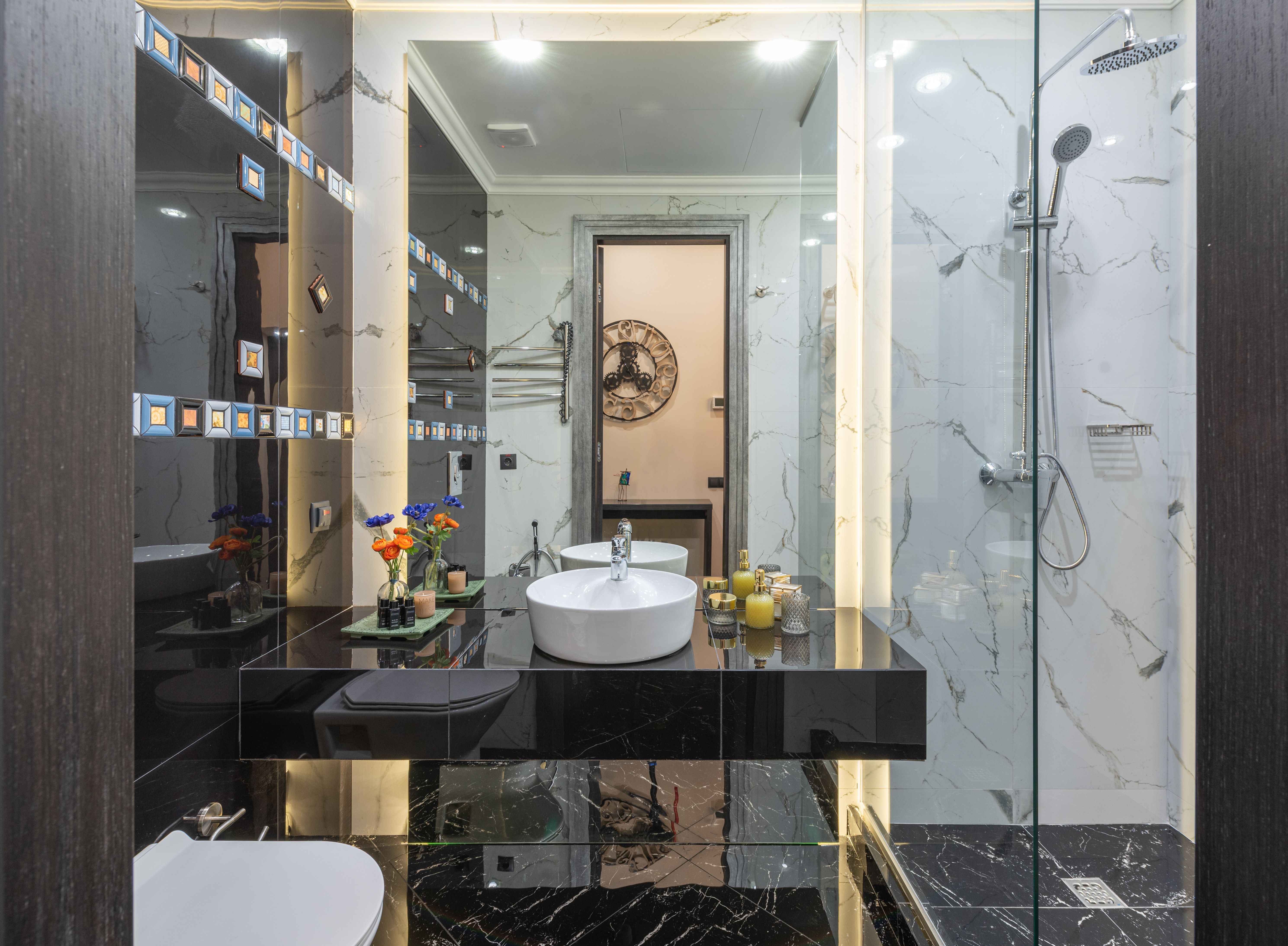 Modern black and white bathroom with vessel sink, backlit mirror and marble shower